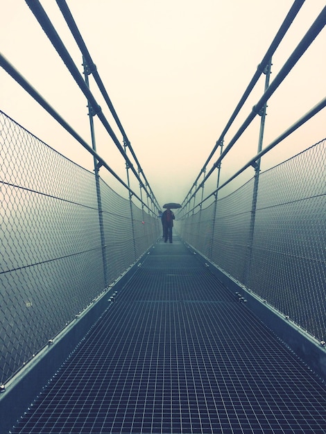 Man staat op een voetgangersbrug tegen de lucht.