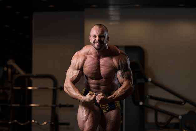 Man staat sterk in de sportschool en buigt spieren Gespierde atletische bodybuilder Fitness Model poseren na oefeningen