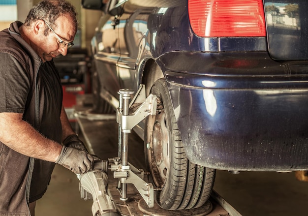 Man staat tijdens het repareren van de stuuruitlijning van een blauwe auto in de garage van een monteur