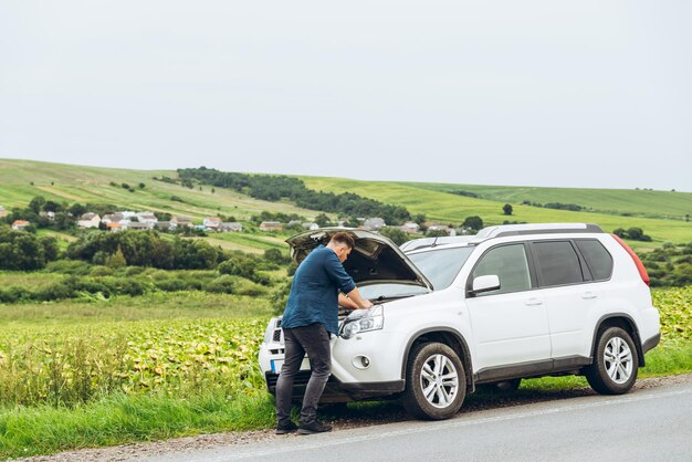 男は開いたフードで壊れた車の近くに立っています。緊急サービス。失敗したロードトリップ