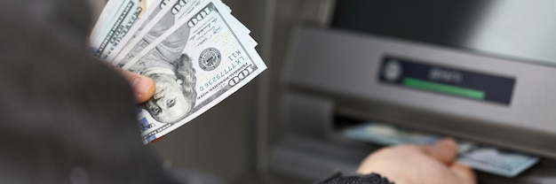 Man stand near terminal and withdraws cash dollars. Limit cash withdrawals during quarantine. Automated cash withdrawal using payment cards. Payment for goods and services through an ATM