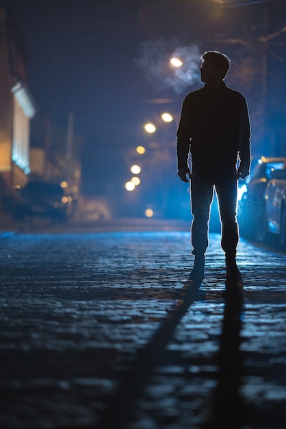 男は雨道に立っている。夕方の夜。望遠レンズ撮影