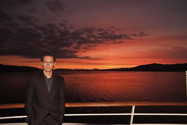 Man stand on ship deck on dramatic sky over sea in Bergen Norway Businessman enjoy sea travel in evening Business or pleasure trip Summer sea vacation Adventure and wanderlust Sunset or sunrise