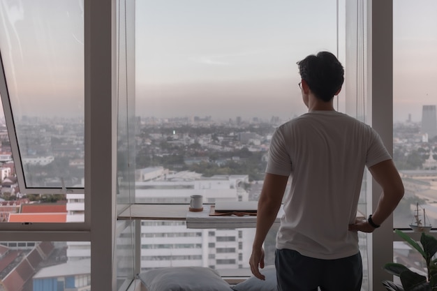 Man stand at the window of the apartment looking out to the city view