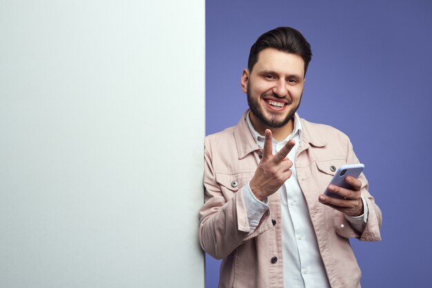 Man standing alongside empty white billboard wall and showing peace gesture