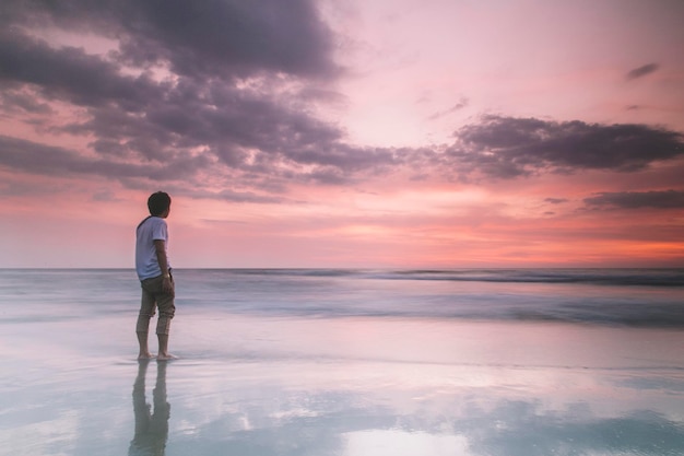 写真 夕暮れの際にビーチに立っている男性