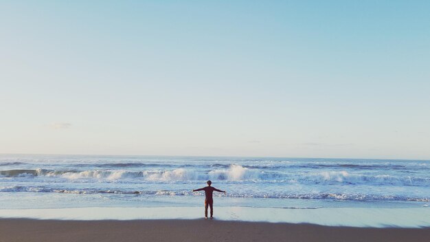 Uomo in piedi sulla spiaggia contro un cielo limpido