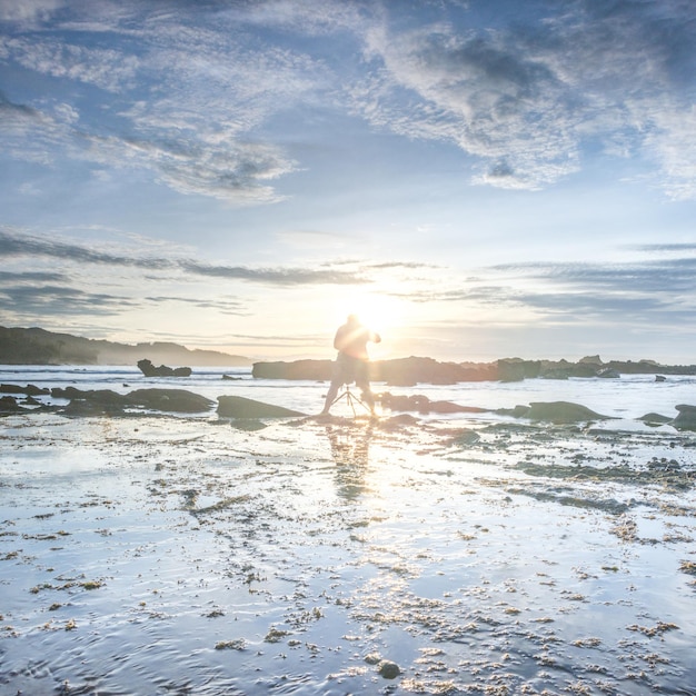 Foto uomo in piedi sulla spiaggia al tramonto