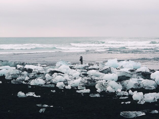 Foto uomo in piedi sulla spiaggia circondato da ghiaccio contro il cielo