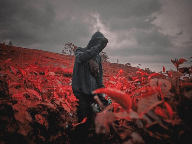 Foto uomo in piedi con l'ombrello rosso contro il cielo durante l'autunno