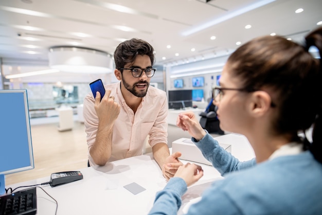 Photo man standing on cashier and complaining for new smart phone while worker listening to him