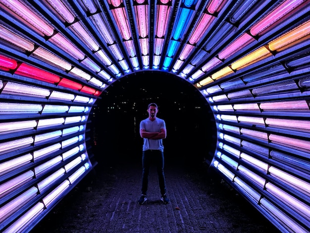 Photo man standing in colorful illuminated tunnel at night