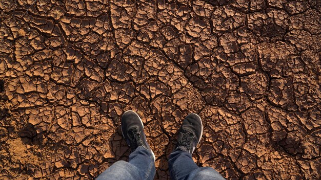 Мужчина, стоящий на сухом потрескавшемся фоне, смотрит сверху на последствия глобального потепления