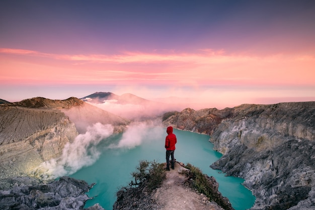 Photo man standing on edge of crater with colorful sky at morning