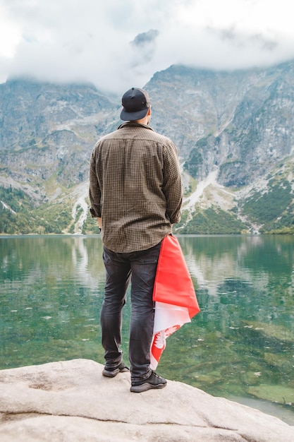 ポケットにポーランドの旗を持ってタトラ山脈の湖を見て端に立っている男