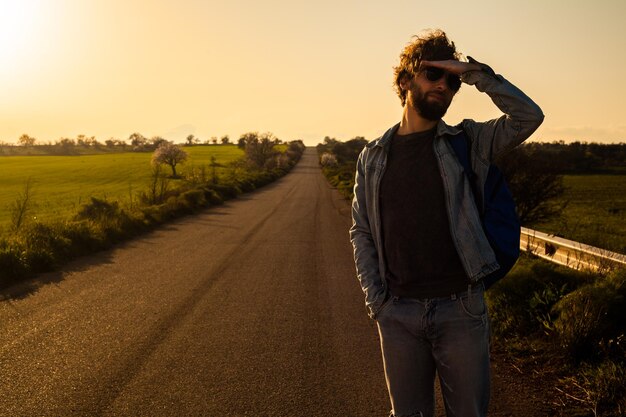 Photo man standing on field by road against sky during sunset