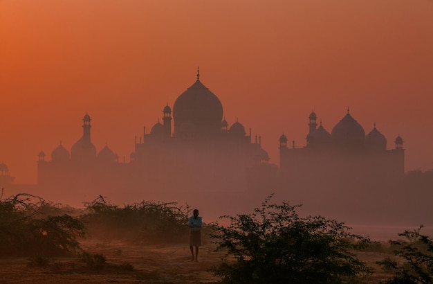 Foto uomo in piedi sul campo con la silhouette del taj mahal sullo sfondo durante l'alba