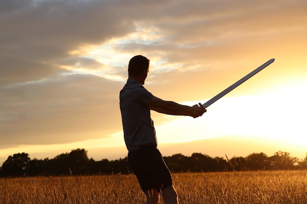 Photo man standing on field with sword against sky during sunset