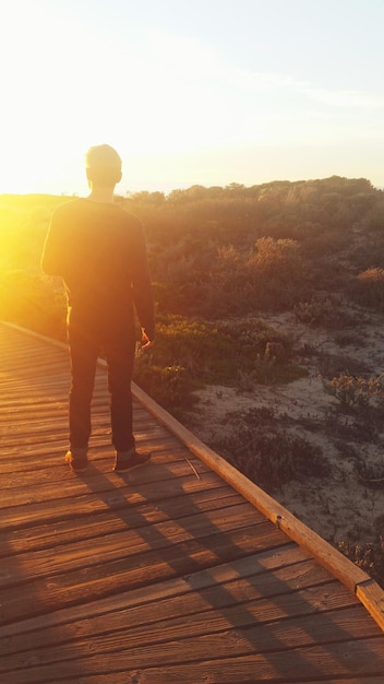 Foto uomo in piedi sul ponte pedonale sopra la montagna durante il tramonto