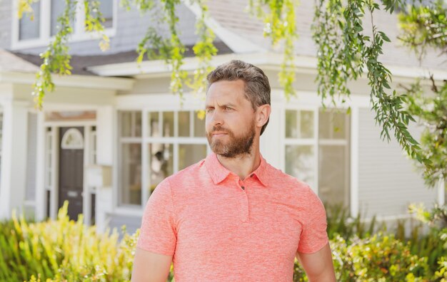 彼の新しい家の前に立っている男。購入、販売、不動産、不動産、住宅保険のコンセプト。現実の人間。晴れた夏の日に屋外に立っているビジネスマン。