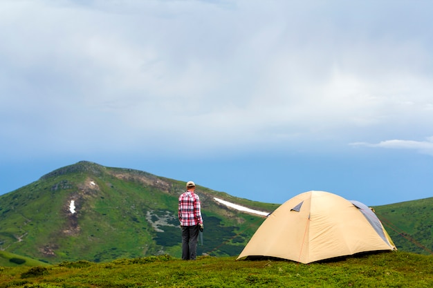 Man standing on green grassy valley at tourist tent