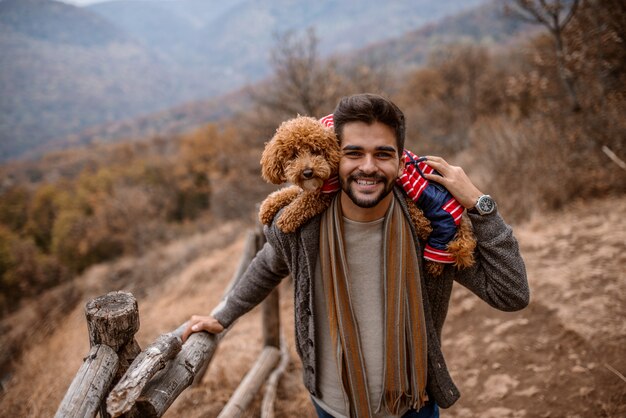 男は立っていると自然の中で肩に犬を保持しています。