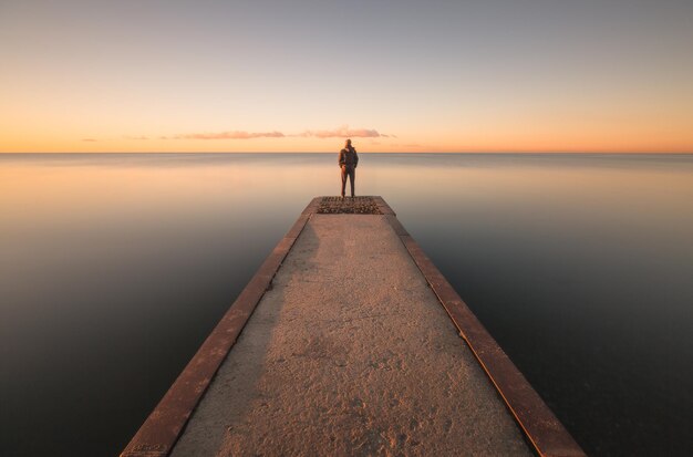 Photo man standing on jetty against sky during sunset