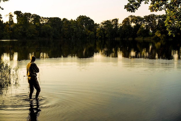 man standing in lake during sunset