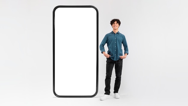 白い背景に巨大な携帯電話の空の画面の近くに立っている男