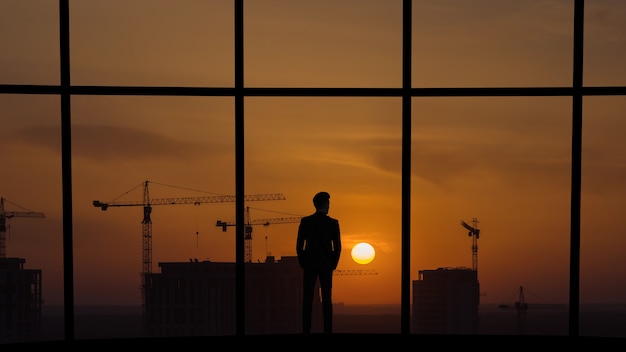 L'uomo in piedi vicino alla finestra panoramica sullo sfondo della costruzione di edifici