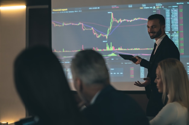 The man standing near the screen on the business meeting