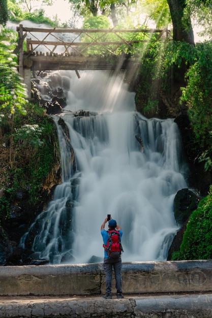 A man standing near the waterfall takes a selfie