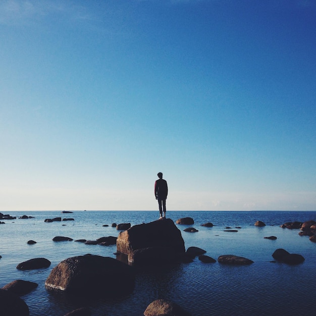 写真 青い空を背景に海を越えて岩の上に立っている男