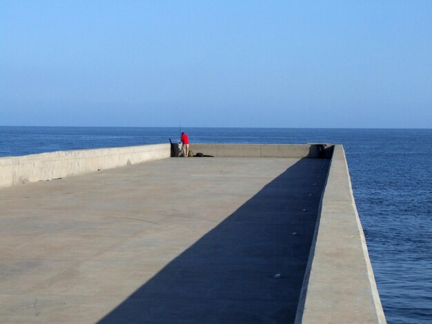 Foto uomo in piedi sul molo sopra il mare contro il cielo blu