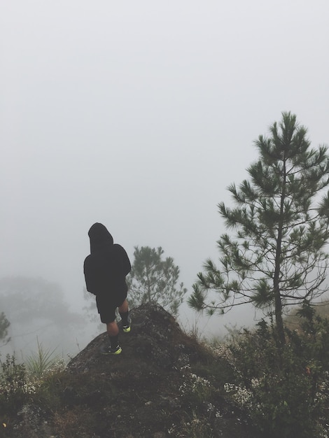 Foto uomo in piedi su una roccia contro il cielo durante il tempo nebbioso