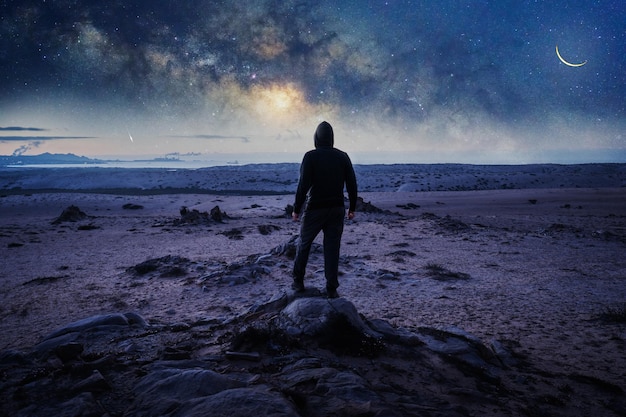 天の川と海の上の星を見つめている岩の後ろの景色に立っている男