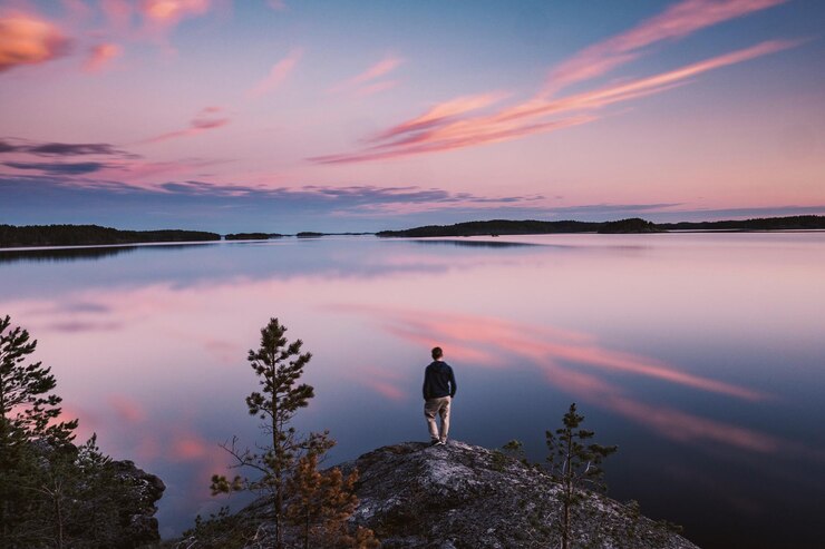 Photo 夕暮れの空に向かって湖のそばの岩の上に立っている男