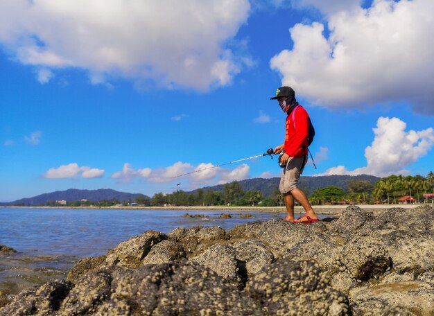 Man standing on rock by mountain against sky