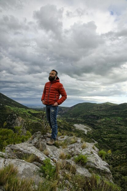 Man standing on rocks by mountains against cloudy sky