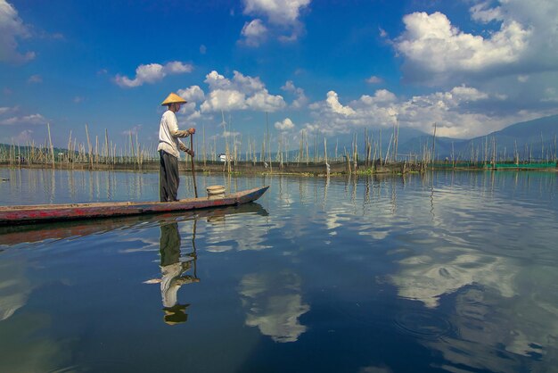 Foto uomo in piedi su una barca a remi nel lago contro il cielo