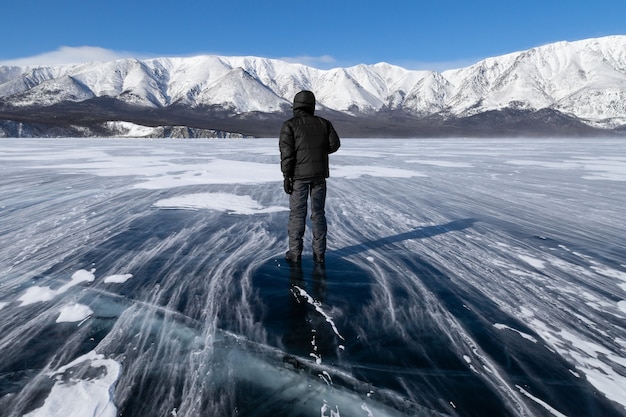 冬の強風の中で凍った山の湖の滑らかな表面に立っている男性。