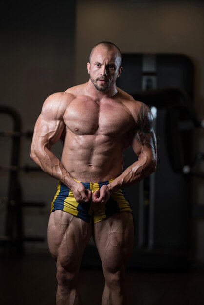 Foto uomo in piedi forte in palestra e flettendo i muscoli modello di fitness bodybuilder atletico muscolare in posa dopo gli esercizi