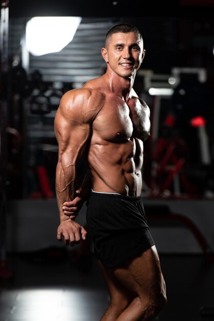 Man Standing Strong In The Gym And Flexing Muscles Muscular Athletic Bodybuilder Fitness Model Posing After Exercises