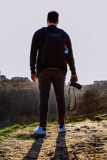 Человек, стоящий на вершине холма на закате, держит камеру в руке фотографа