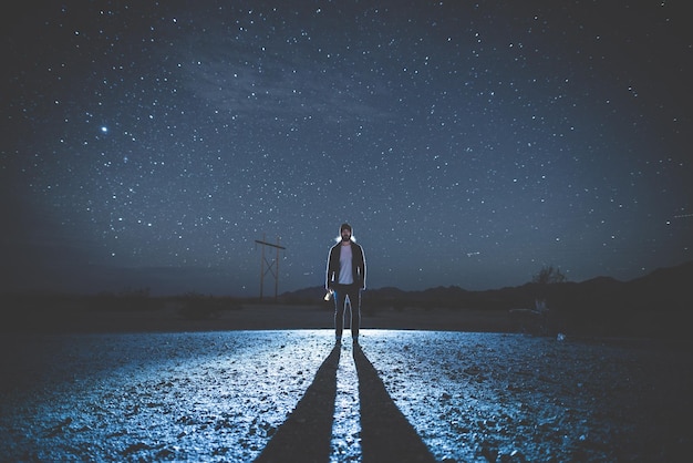 Man standing with long shadow on field against sky at night
