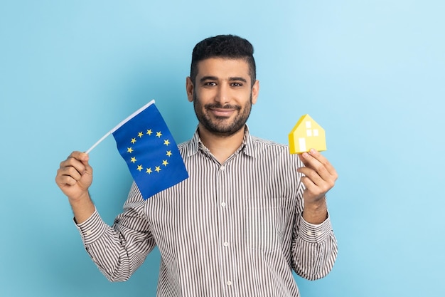 Man standing with paper house and flag of European Union immigration and house purchase in Europe