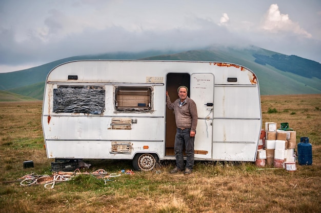 写真 空に向かって山の上に旅行用トレーラーを乗せて立っている男