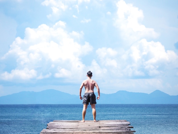 Man standing on wooden bridge into blue sea. 