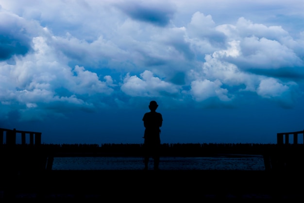 Man standing on a wooden bridge in a sea of darkness.