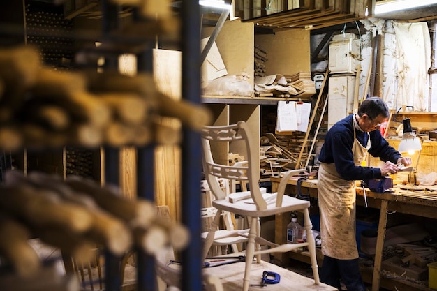 Man standing at a work bench in a carpentry workshop working on a piece of wood secured in a bench